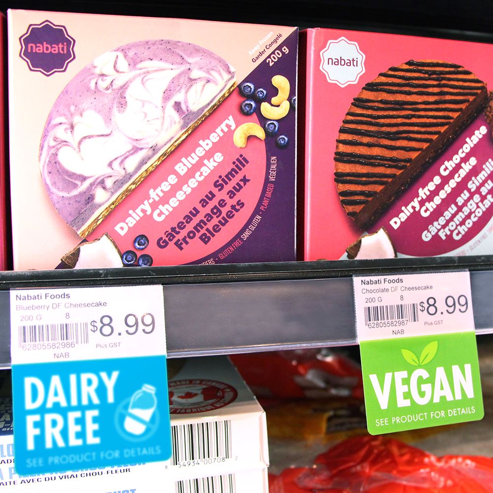 A grocery store freezer with cheesecakes on a shelf edge with "dairy free" and "vegan" ShelfTalkers installed into the ticket molding.