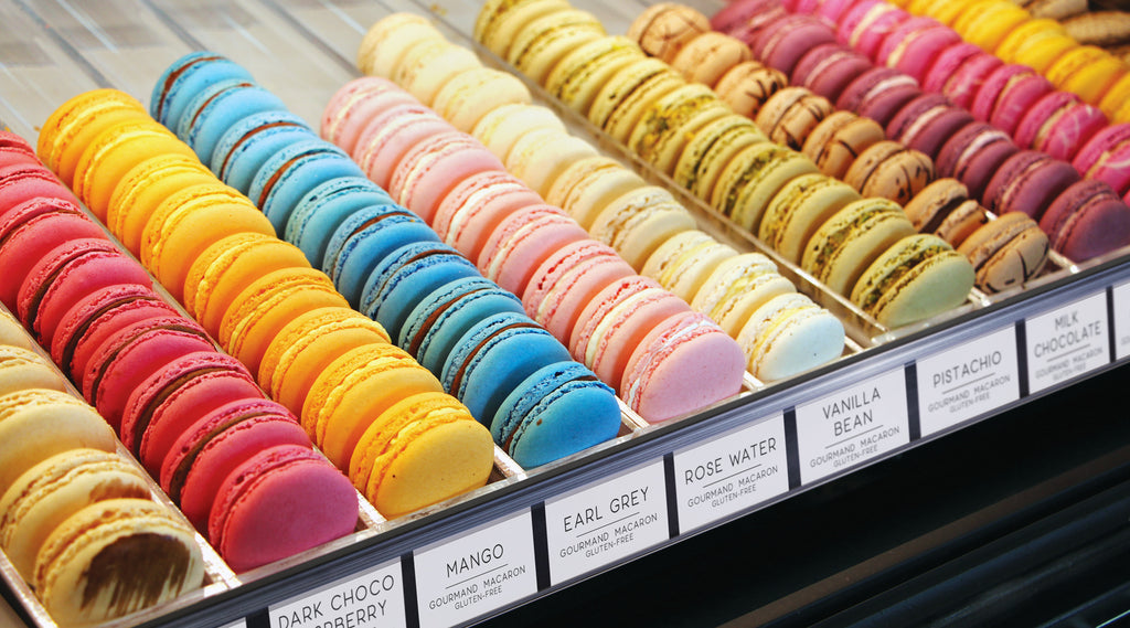 A bakery shelf holding an assortment of macarons with ClearGrip ticket molding on the shelf edge