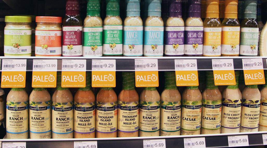 A grocery store shelf edge with bottles of salad dressing and "Paleo" ShelfTalkers displayed below