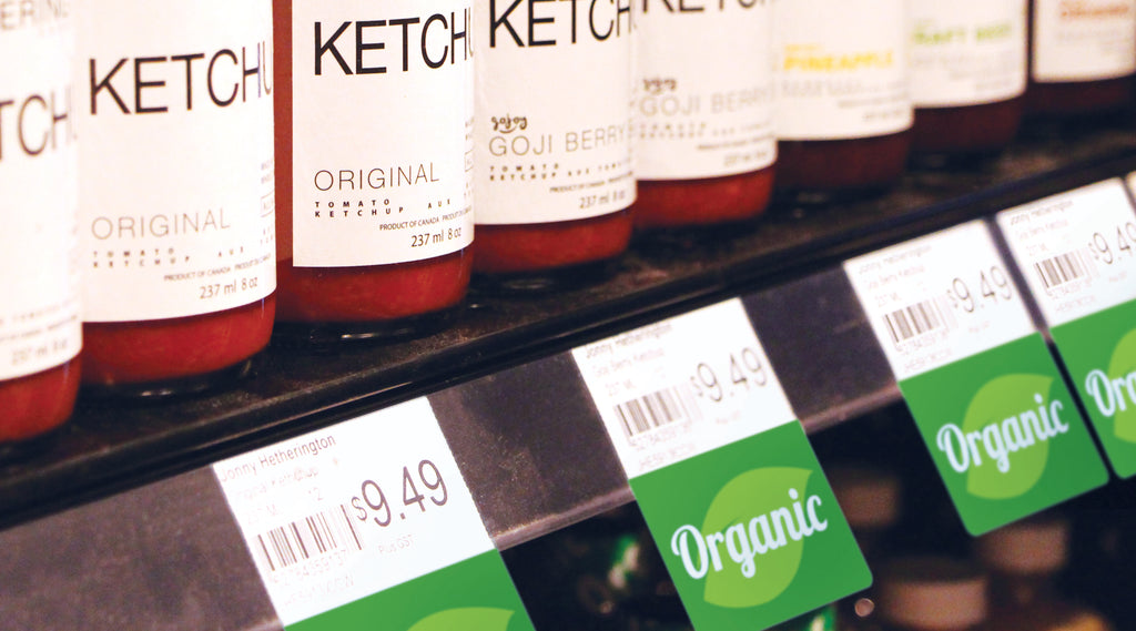 A shelf edge holding bottles of ketchup with "Organic" ShelfTalkers attached underneath