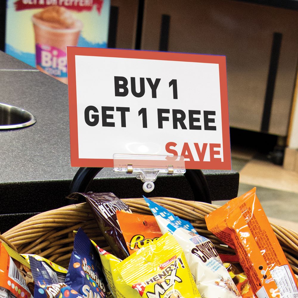 A basket of snacks in a convenience store with the TwistKlip Display Clip with Large Clip clipped to it and holding a large 'BOGO' sign