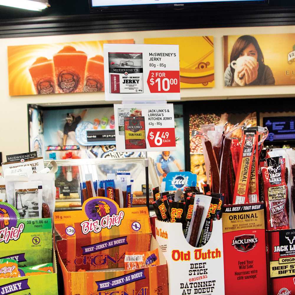 The PowerGrip Three Grip, Center Stem, Adjustable Sign Holder holding signs up displaying prices of beef jerky on a convenience store shelf