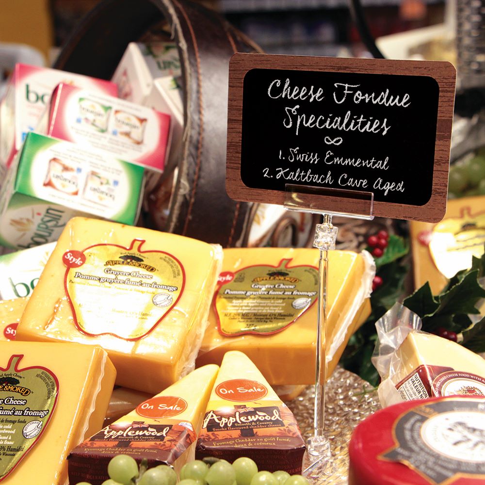 A deli store display with various cheese and a TwistKlip sign holder with a ChalkTalker deli sign