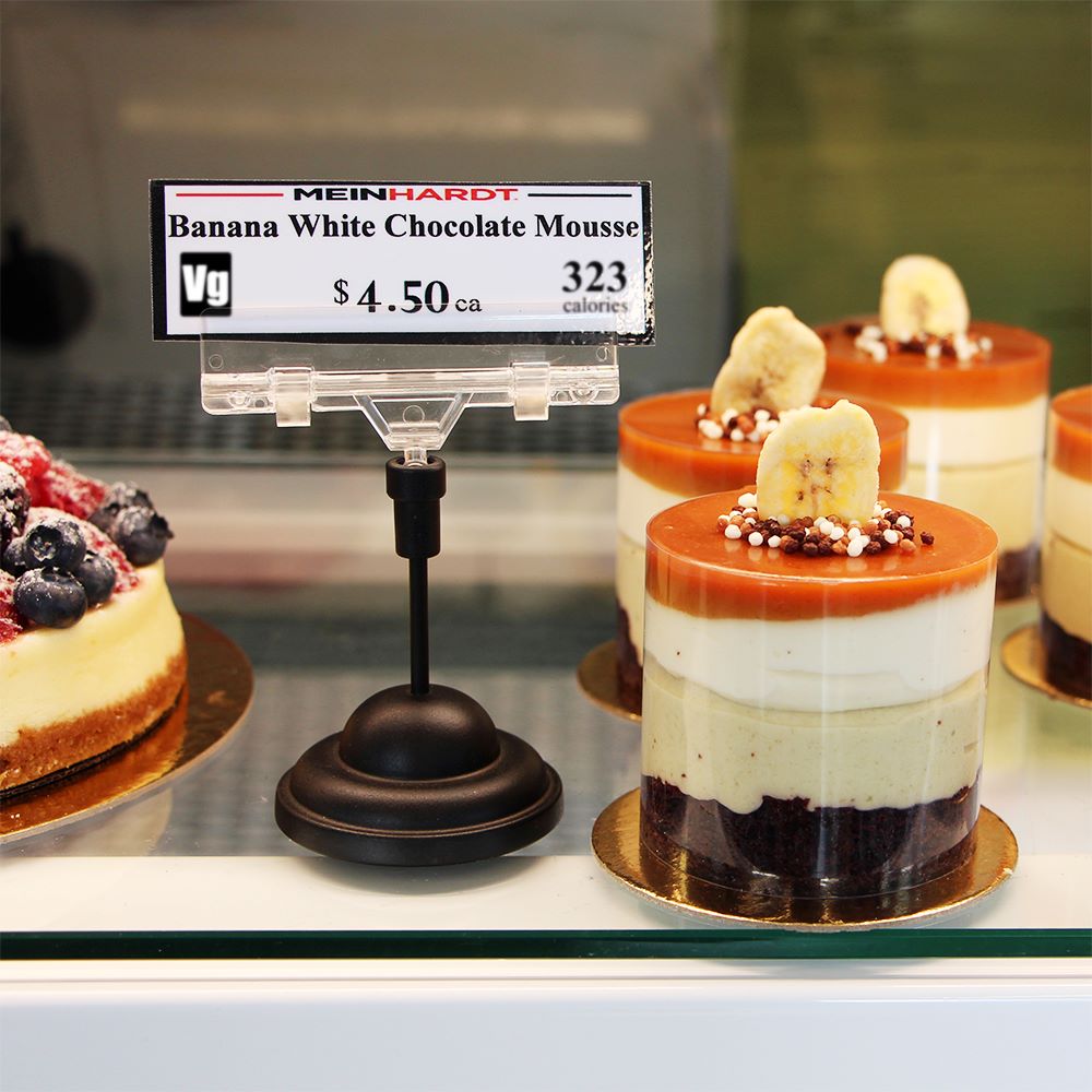 A bakery shelf with individual white chocolate mousse and a Large Sign Clip, Contour Base Sign Holder holding a price sign