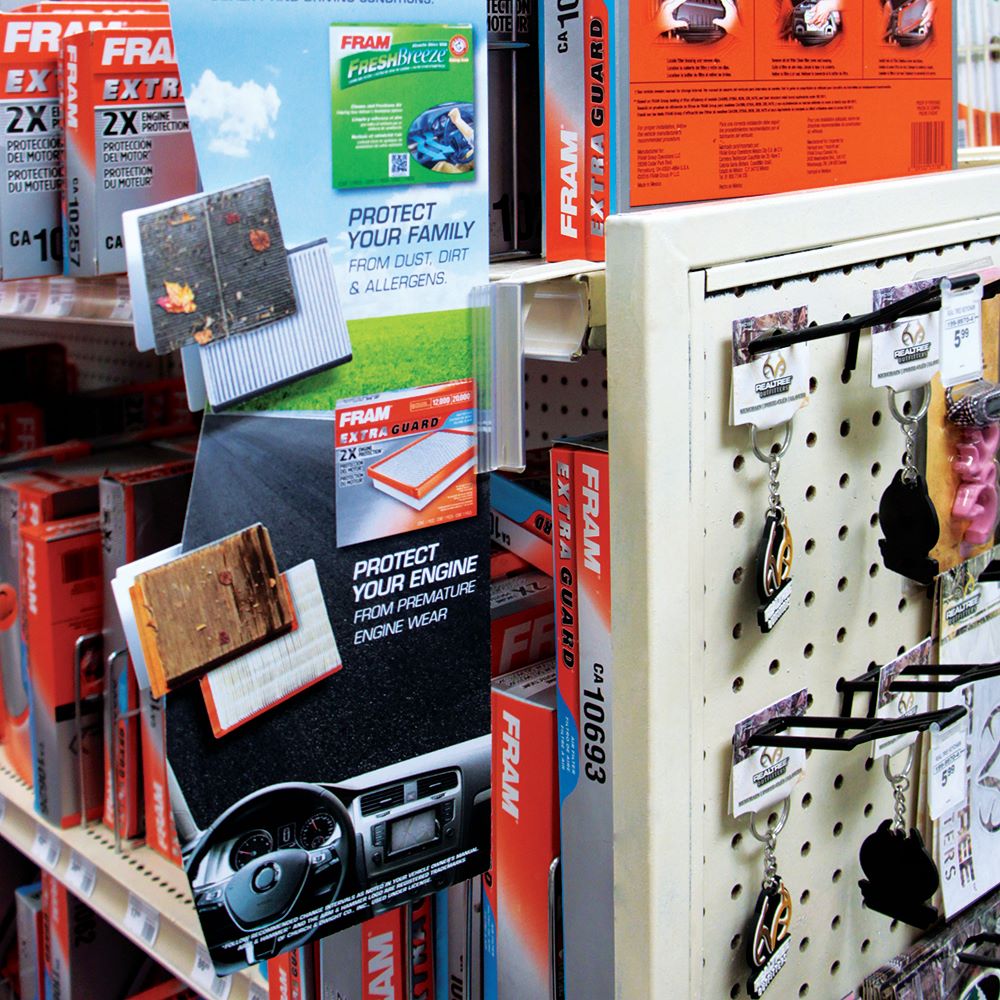 A gas station shelf with the Top Mount, Right Angle, Aisle Sign Holder holding a large vertical promotional sign 