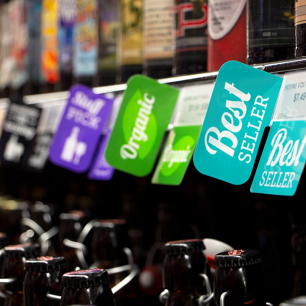 An assortment of colorful ShelfTalkers attached to a liquor store shelf edge.