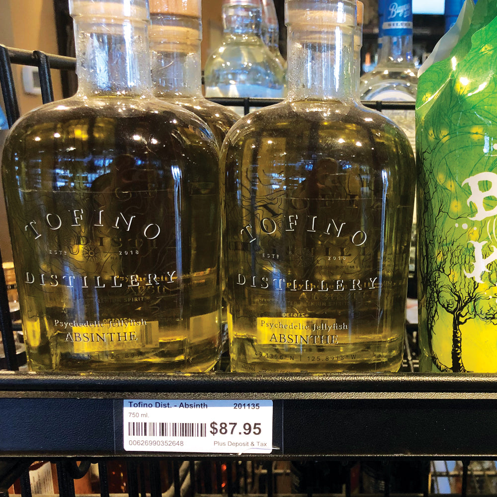 A liquor store shelf edge with bottles of absinthe and a price ticket in the price channel with a piecce of SnipAStrip Price Channel Label Protector covering it