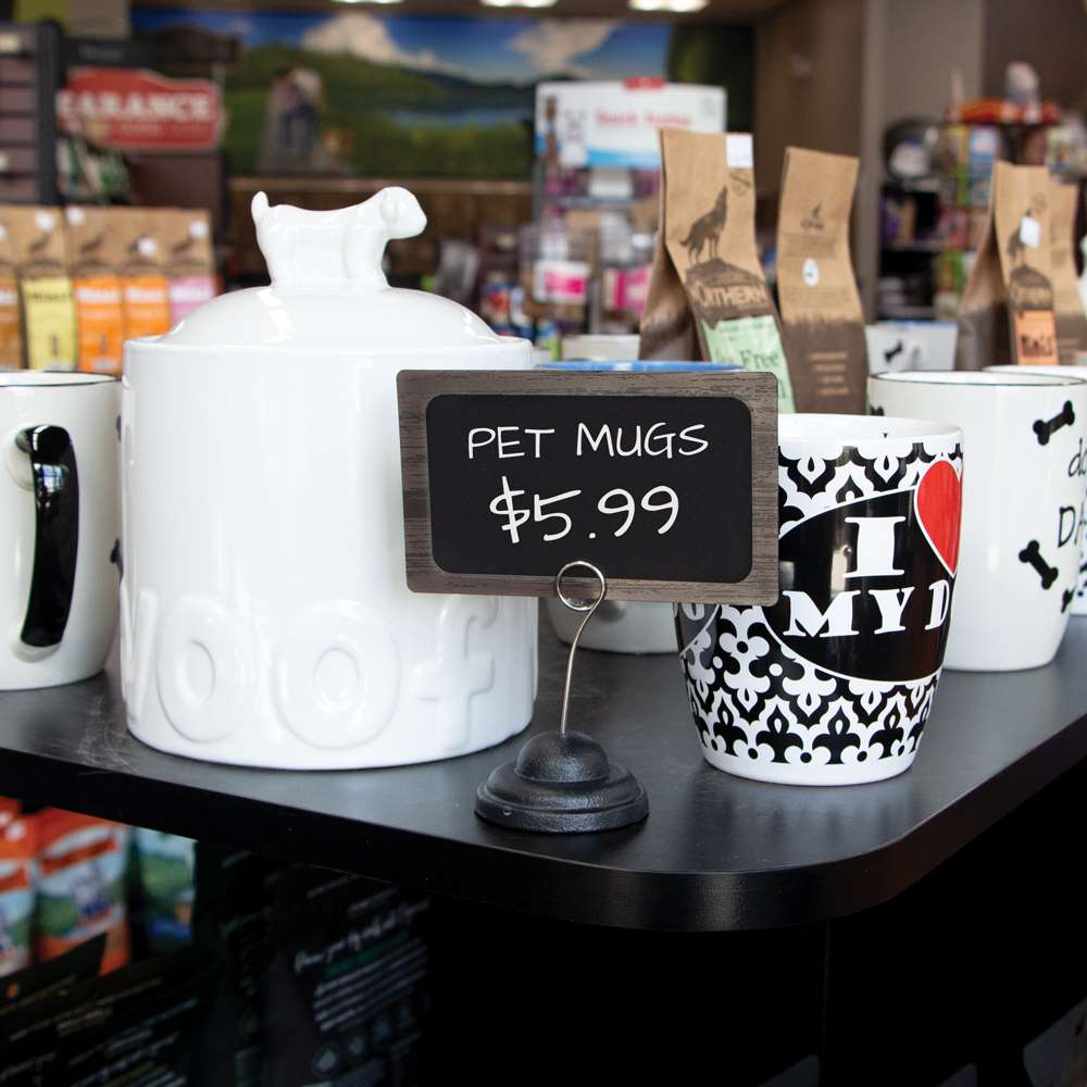 A shelf top with mugs for pet owners and a 3 inch Spiral Clip, Contour Base Sign Holder holding a deli sign ChalkTalker