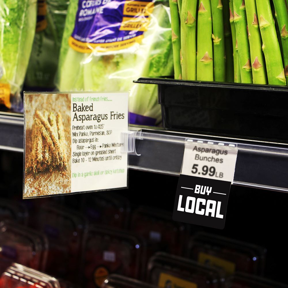 A shelf edge in a produce section with a ClearGrip ticket molding with a "Buy Local" ShelfTalker and a right angle sign clip with PowerGrip holding a sign.