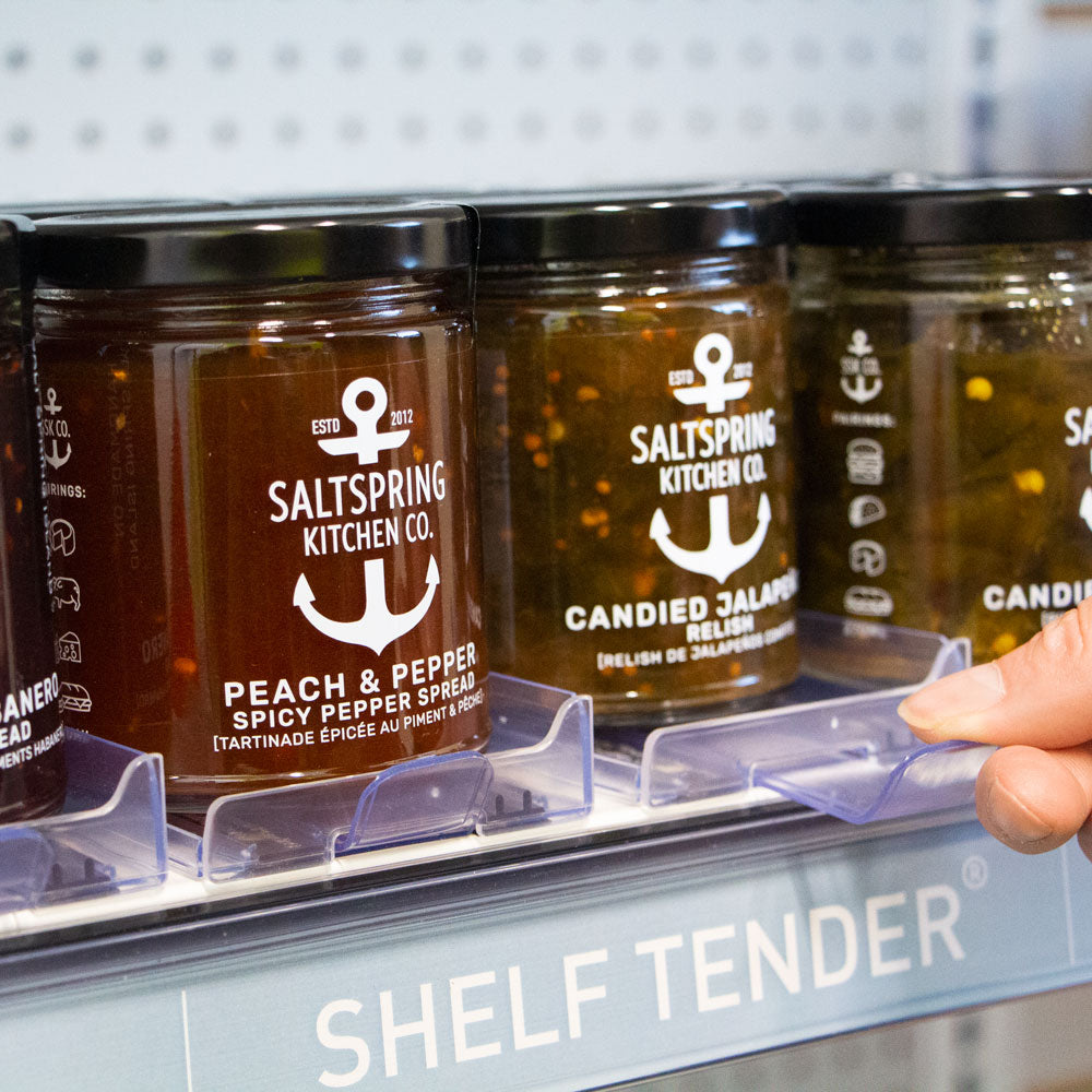 Glass jars of jellies and condiments on a medium sized Shelf Tender being pulled forward via the Shelf Tender puller.