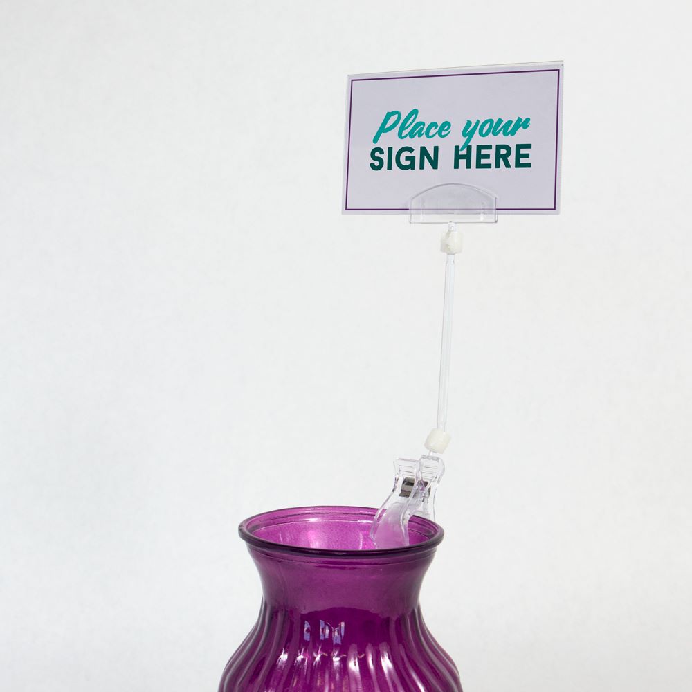 The TwistKlip Card Holder with Large Clip, Long Extension clipped onto a vase and gripping a sign