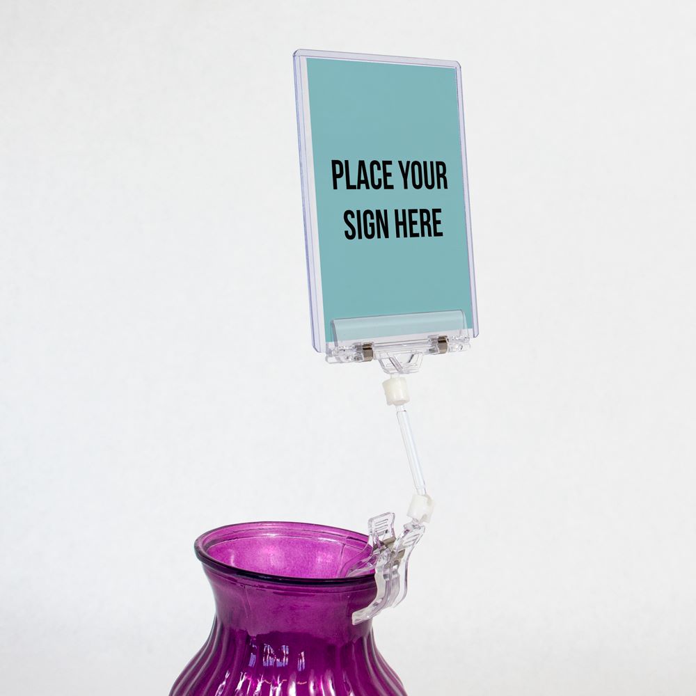 The TwistKlip Wide Card Holder with Small Clip in clear clipped to a vase and holding a sign protector containing a sign