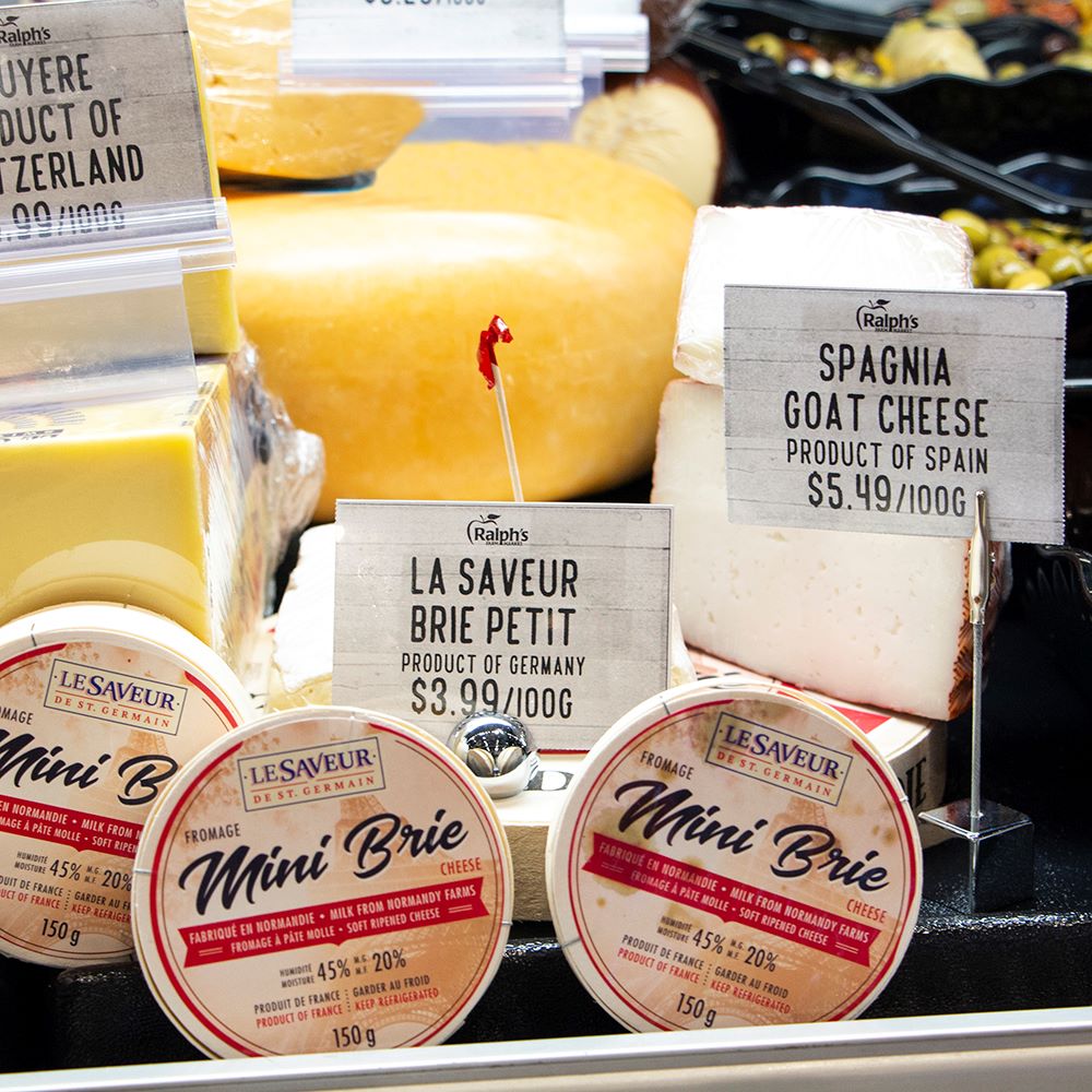 An assortment of cheeses in a deli case with tabletop sign holders displaying signs with prices.