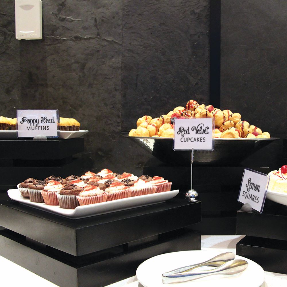 A fancy display of baked goods at an event with table top sign holders displaying signs.